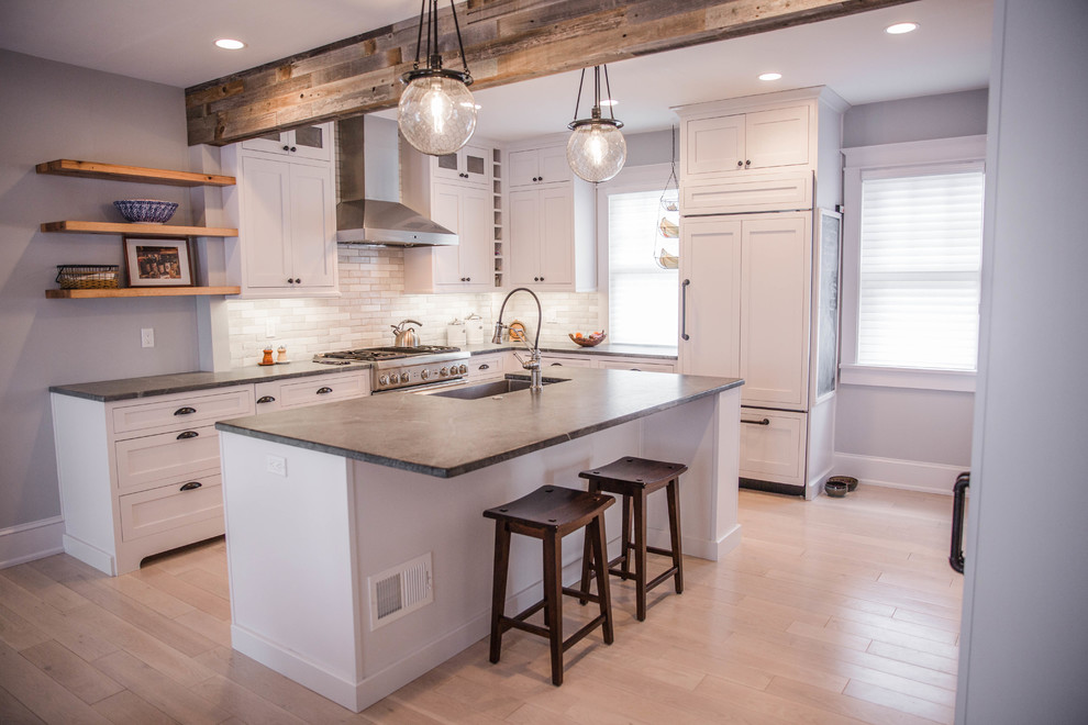 Example of a mid-sized cottage l-shaped limestone floor eat-in kitchen design in Philadelphia with a farmhouse sink, shaker cabinets, white cabinets, soapstone countertops, ceramic backsplash, stainless steel appliances and an island