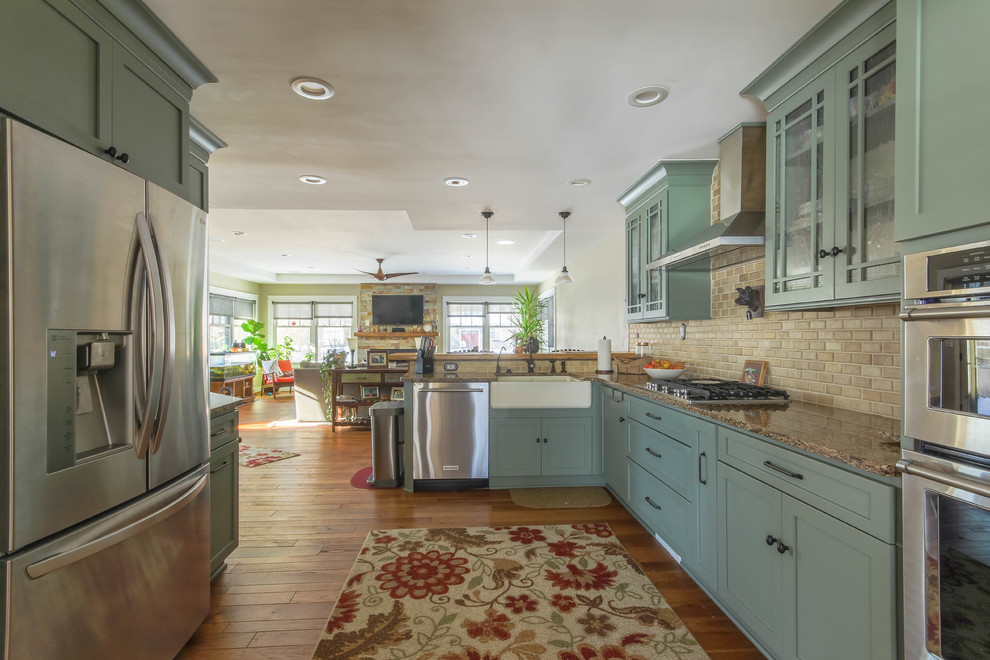 Inspiration for a large country u-shaped medium tone wood floor and brown floor eat-in kitchen remodel in Detroit with a farmhouse sink, shaker cabinets, green cabinets, quartz countertops, beige backsplash, travertine backsplash, stainless steel appliances, a peninsula and brown countertops