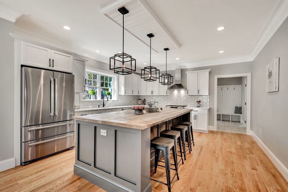 Example of a cottage l-shaped medium tone wood floor and brown floor kitchen design in Boston with shaker cabinets, white cabinets, wood countertops, white backsplash, stainless steel appliances, an island and beige countertops