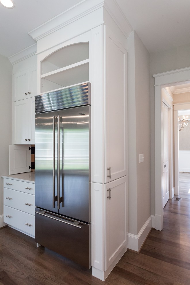 Farmhouse l-shaped open plan kitchen in DC Metro with a belfast sink, recessed-panel cabinets, white cabinets, white splashback, metro tiled splashback, stainless steel appliances, medium hardwood flooring, an island, brown floors and white worktops.