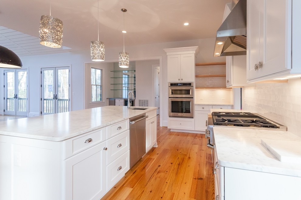 Open concept kitchen - country u-shaped light wood floor open concept kitchen idea in DC Metro with a farmhouse sink, shaker cabinets, white cabinets, white backsplash, subway tile backsplash, stainless steel appliances, white countertops and an island