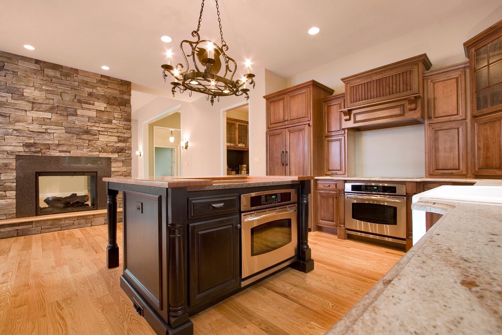 Medium sized traditional l-shaped open plan kitchen in Other with raised-panel cabinets, medium wood cabinets, granite worktops, stainless steel appliances, light hardwood flooring and an island.