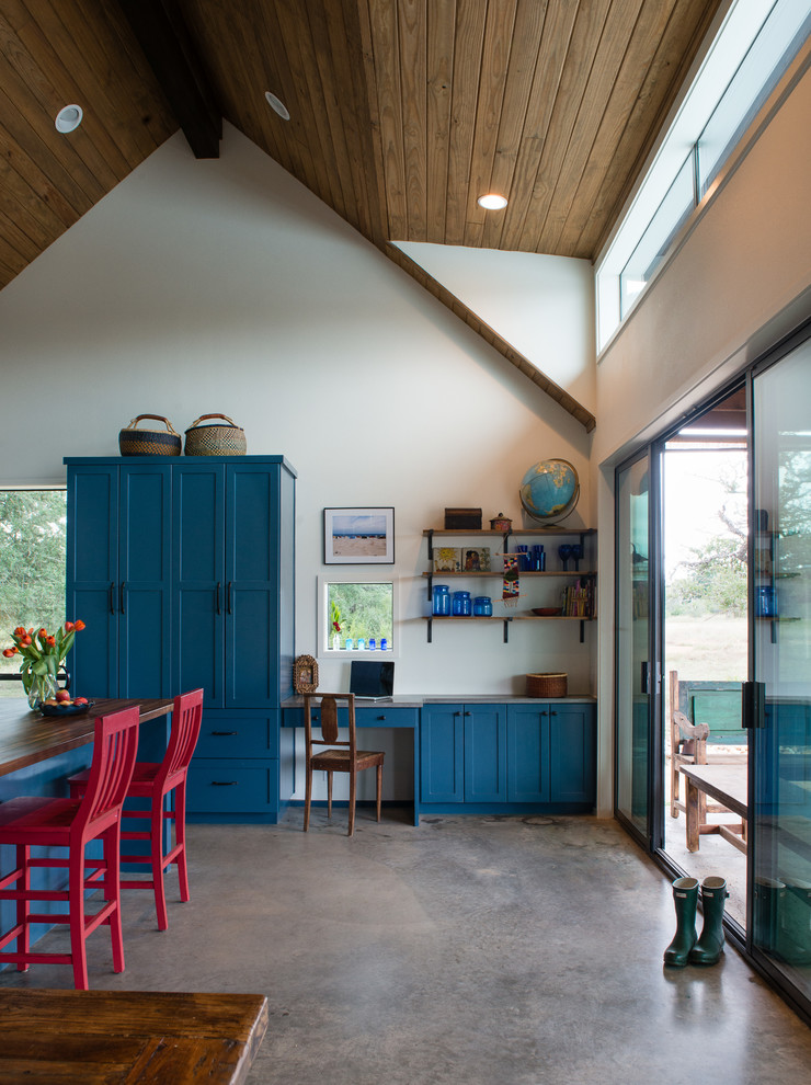 Modelo de cocina de estilo de casa de campo abierta con armarios estilo shaker, puertas de armario azules, suelo de cemento y una isla