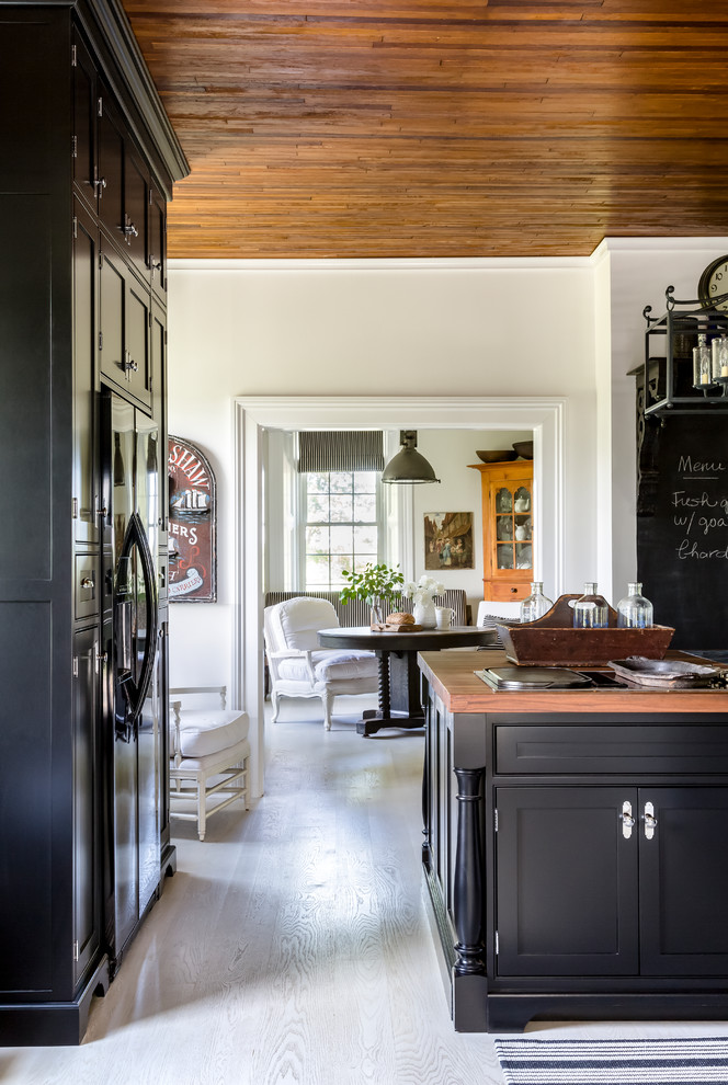 This is an example of a rural kitchen in Other with a belfast sink, black cabinets, black appliances, painted wood flooring, an island and white floors.