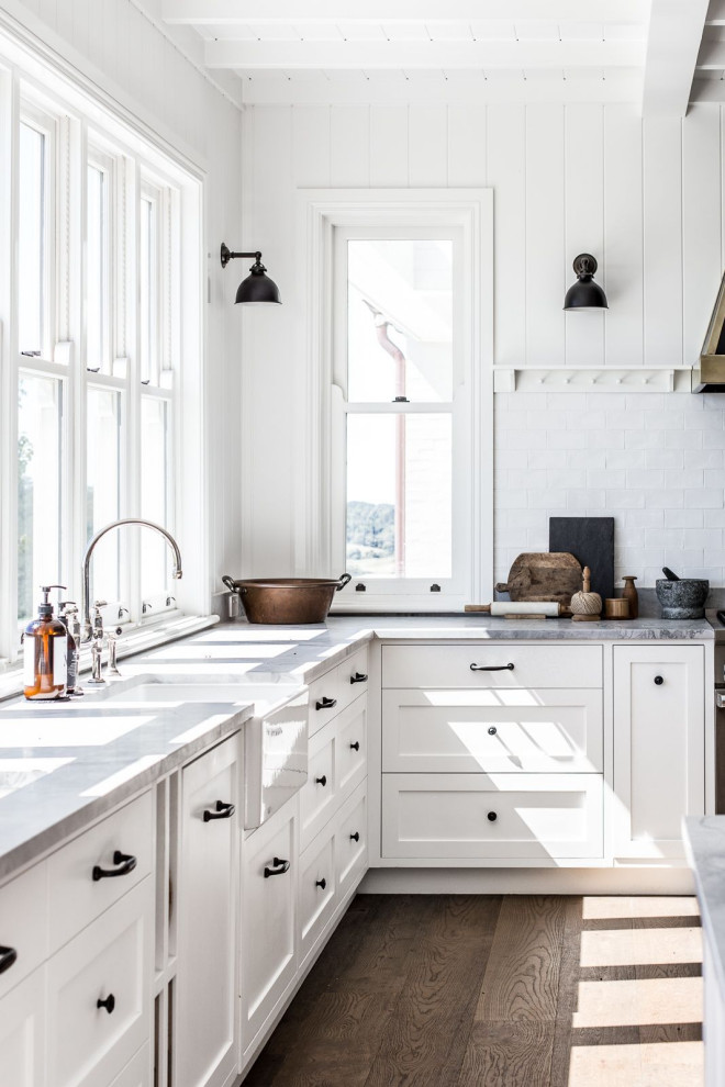 Bild på ett stort lantligt grå grått kök, med en rustik diskho, vita skåp, marmorbänkskiva, vitt stänkskydd, stänkskydd i tunnelbanekakel, rostfria vitvaror, mellanmörkt trägolv, en köksö, brunt golv och skåp i shakerstil