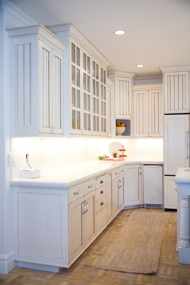 Example of a large farmhouse u-shaped brick floor eat-in kitchen design in Salt Lake City with an undermount sink, beaded inset cabinets, white cabinets, marble countertops, white backsplash, subway tile backsplash, white appliances and an island