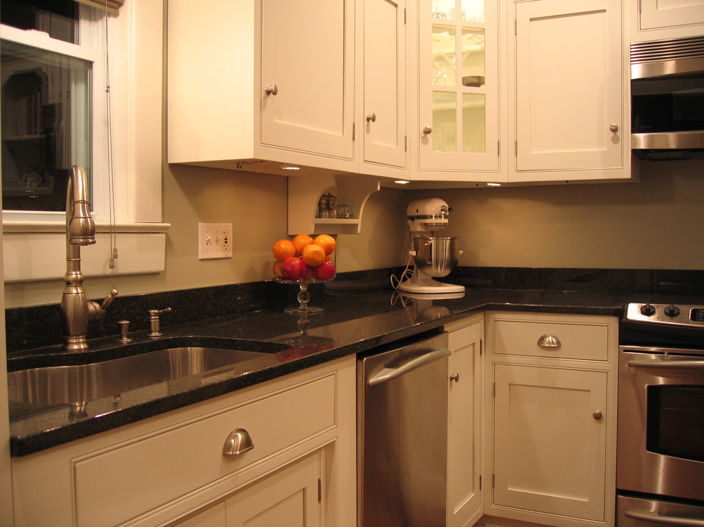 Example of a small farmhouse l-shaped light wood floor enclosed kitchen design in Denver with an undermount sink, flat-panel cabinets, white cabinets, granite countertops, stainless steel appliances and an island