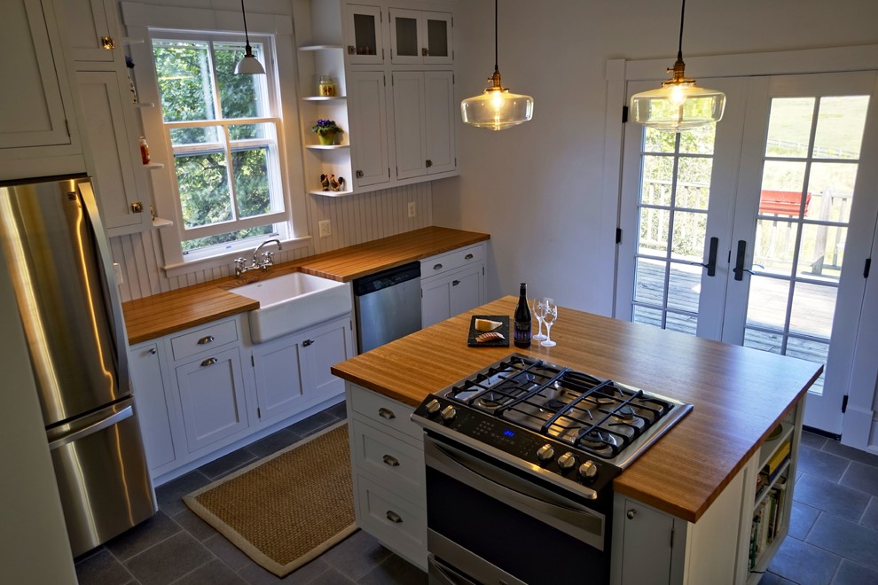 Foto på ett mellanstort lantligt brun kök och matrum, med en undermonterad diskho, vita skåp, träbänkskiva, brunt stänkskydd, rostfria vitvaror, klinkergolv i porslin, en köksö och grått golv