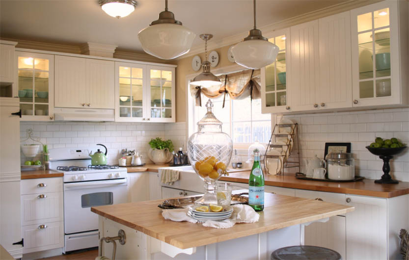 Eat-in kitchen - mid-sized traditional l-shaped vinyl floor eat-in kitchen idea in Los Angeles with a farmhouse sink, glass-front cabinets, white cabinets, wood countertops, white backsplash, subway tile backsplash, white appliances and an island
