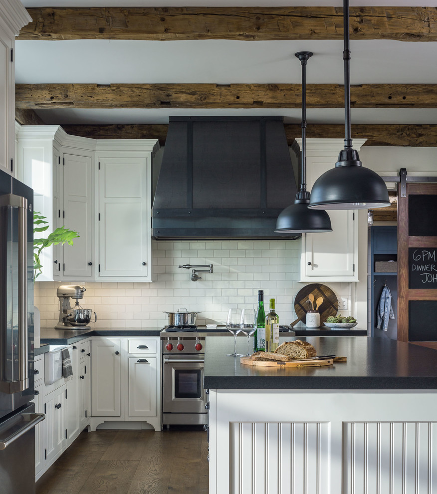 Inspiration for a mid-sized cottage u-shaped medium tone wood floor and brown floor eat-in kitchen remodel in Other with a farmhouse sink, recessed-panel cabinets, white cabinets, granite countertops, white backsplash, subway tile backsplash, stainless steel appliances, an island and black countertops