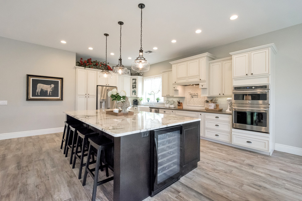Inspiration for a large farmhouse l-shaped porcelain tile and gray floor open concept kitchen remodel in Phoenix with a farmhouse sink, raised-panel cabinets, white cabinets, granite countertops, white backsplash, subway tile backsplash, stainless steel appliances and an island