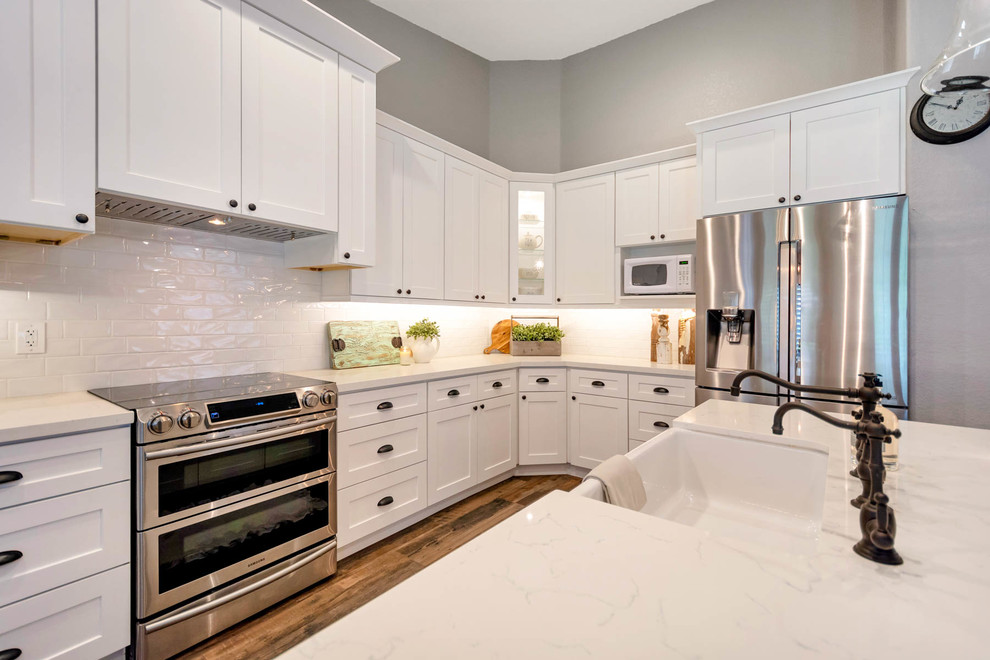 Example of a large farmhouse l-shaped open concept kitchen design in Phoenix with a farmhouse sink, shaker cabinets, white cabinets, quartz countertops, white backsplash, subway tile backsplash, stainless steel appliances, an island and white countertops