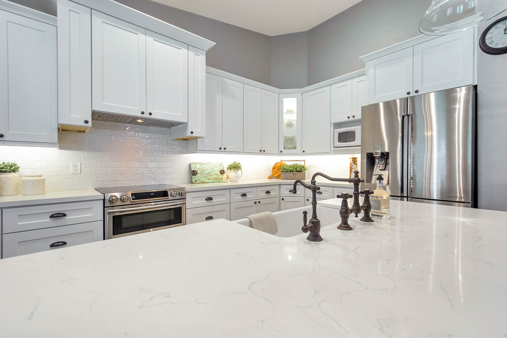 Example of a large country l-shaped open concept kitchen design in Phoenix with a farmhouse sink, shaker cabinets, white cabinets, quartz countertops, white backsplash, subway tile backsplash, stainless steel appliances, an island and white countertops