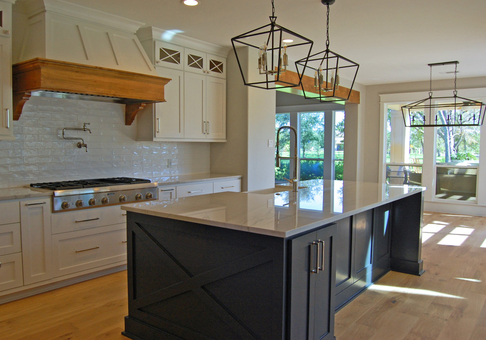 Example of a large cottage u-shaped light wood floor and beige floor eat-in kitchen design in Houston with a farmhouse sink, shaker cabinets, white cabinets, quartzite countertops, white backsplash, ceramic backsplash, stainless steel appliances, an island and white countertops