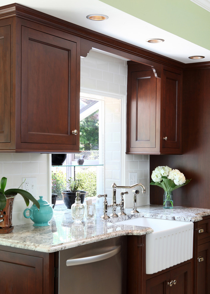 Klassisk inredning av ett mellanstort kök, med en rustik diskho, luckor med infälld panel, skåp i mörkt trä, granitbänkskiva, vitt stänkskydd, stänkskydd i tunnelbanekakel, rostfria vitvaror, klinkergolv i porslin, en halv köksö och beiget golv