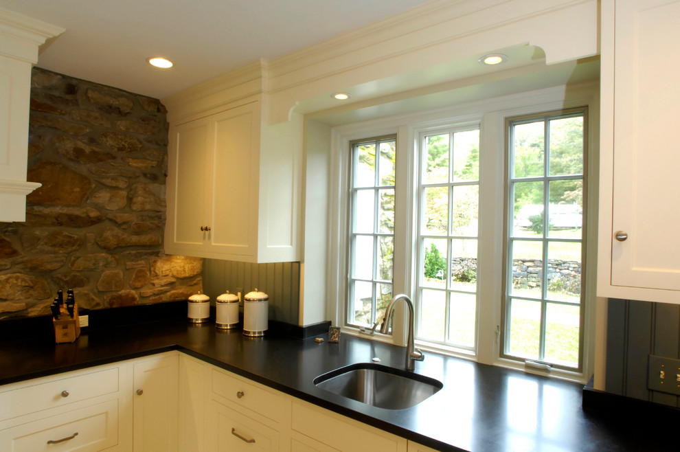Immagine di una cucina country di medie dimensioni con lavello sottopiano, ante a filo, ante bianche, top in granito, paraspruzzi blu, elettrodomestici da incasso e pavimento in travertino
