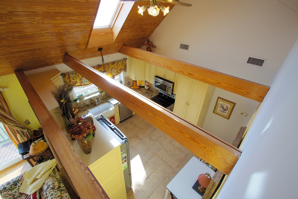 Landhaus Wohnküche mit Landhausspüle, gelben Schränken, Granit-Arbeitsplatte und Küchengeräten aus Edelstahl in Sonstige