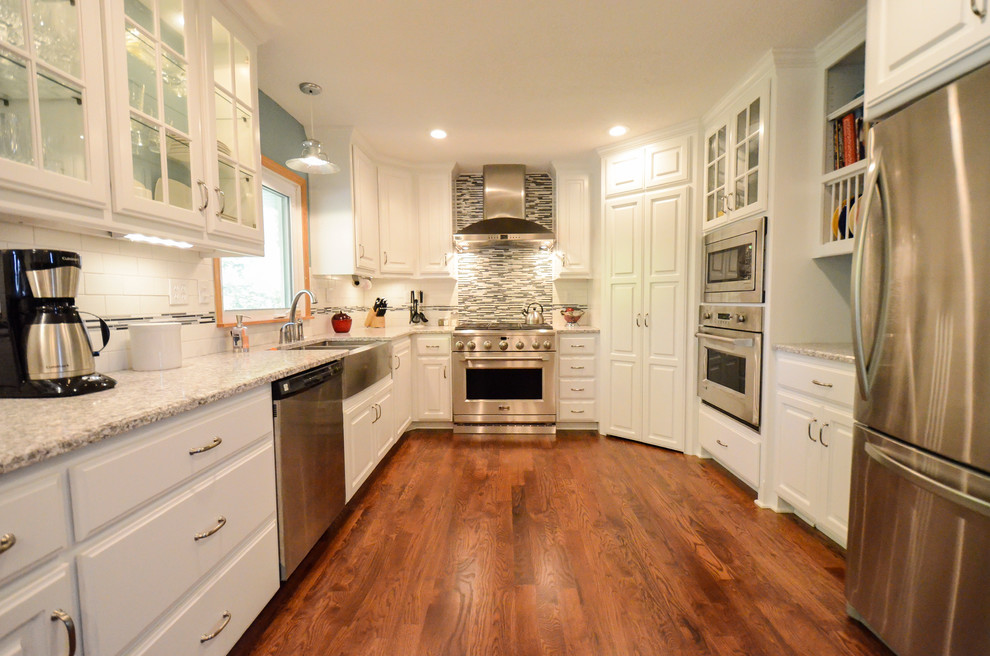 Example of a large classic u-shaped medium tone wood floor eat-in kitchen design in Kansas City with a farmhouse sink, raised-panel cabinets, white cabinets, quartz countertops, multicolored backsplash, mosaic tile backsplash, stainless steel appliances and no island