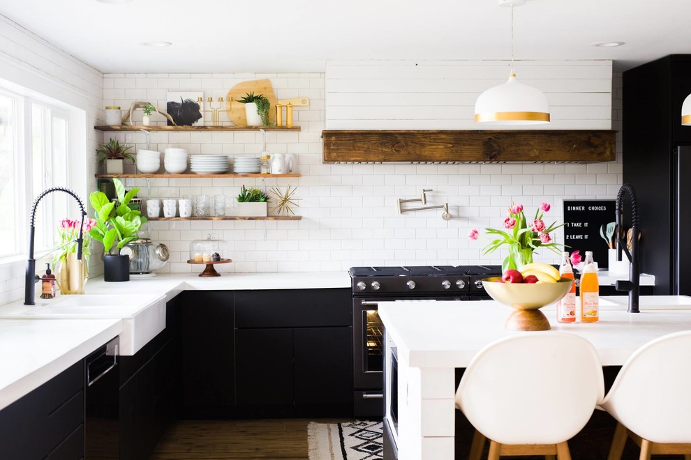 Inspiration for a large rural l-shaped kitchen/diner in Other with a belfast sink, flat-panel cabinets, black cabinets, concrete worktops, white splashback, ceramic splashback, black appliances, laminate floors, an island, brown floors and white worktops.