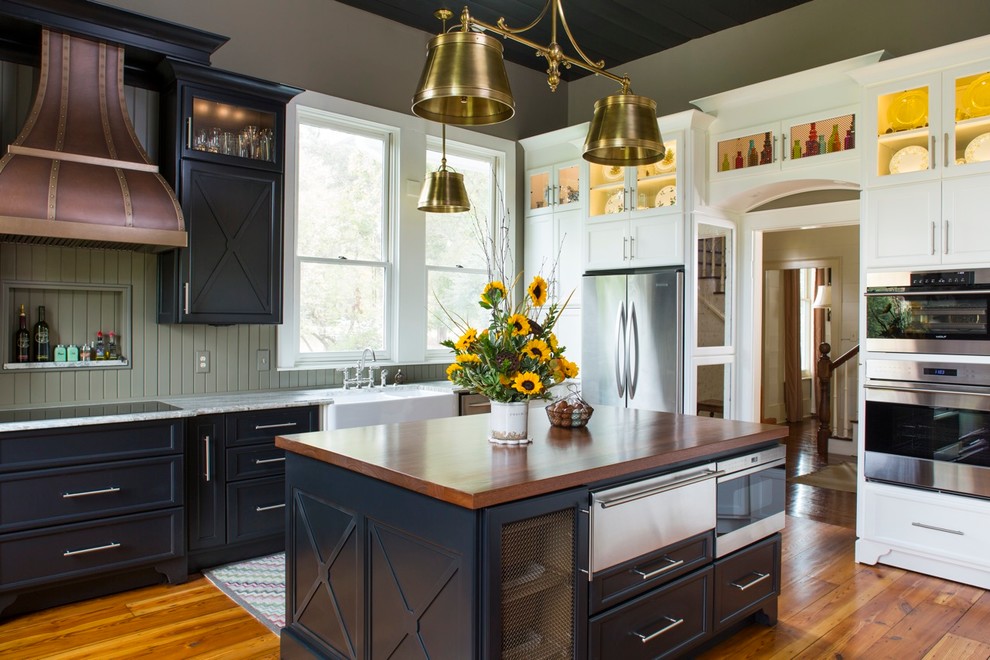 Inspiration for a large farmhouse u-shaped medium tone wood floor enclosed kitchen remodel in Atlanta with a farmhouse sink, recessed-panel cabinets, black cabinets, wood countertops, green backsplash, stainless steel appliances and an island