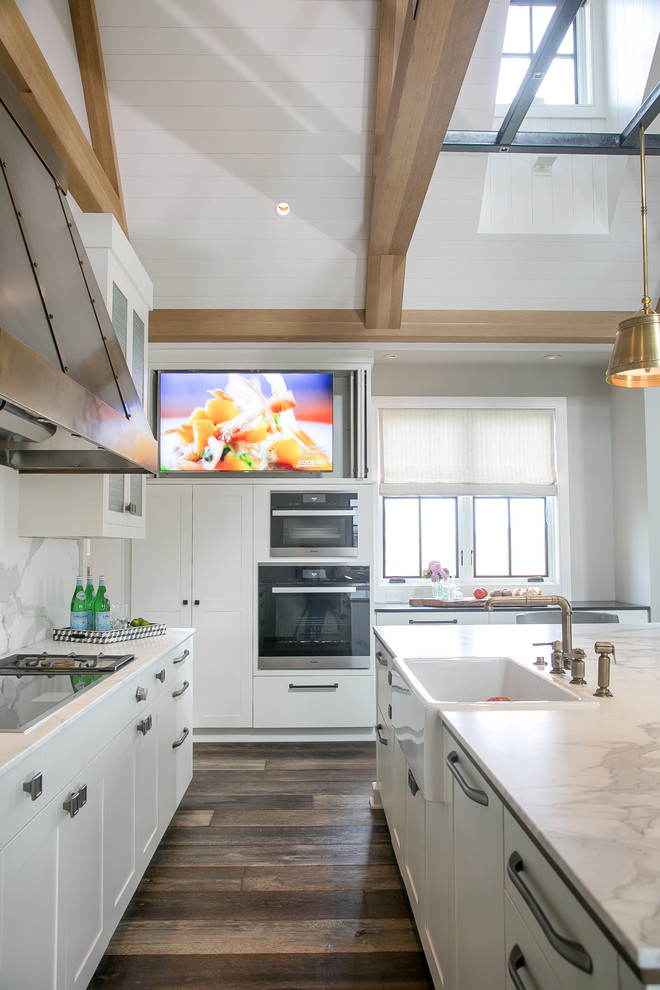 Inspiration for an expansive farmhouse u-shaped open plan kitchen in Milwaukee with a belfast sink, recessed-panel cabinets, white cabinets, engineered stone countertops, multi-coloured splashback, black appliances, dark hardwood flooring, an island, stone slab splashback and brown floors.