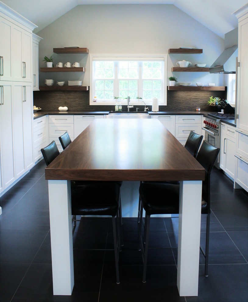 Medium sized country u-shaped kitchen/diner in Boston with a belfast sink, shaker cabinets, white cabinets, composite countertops, black splashback, porcelain splashback, integrated appliances, ceramic flooring, an island and black floors.