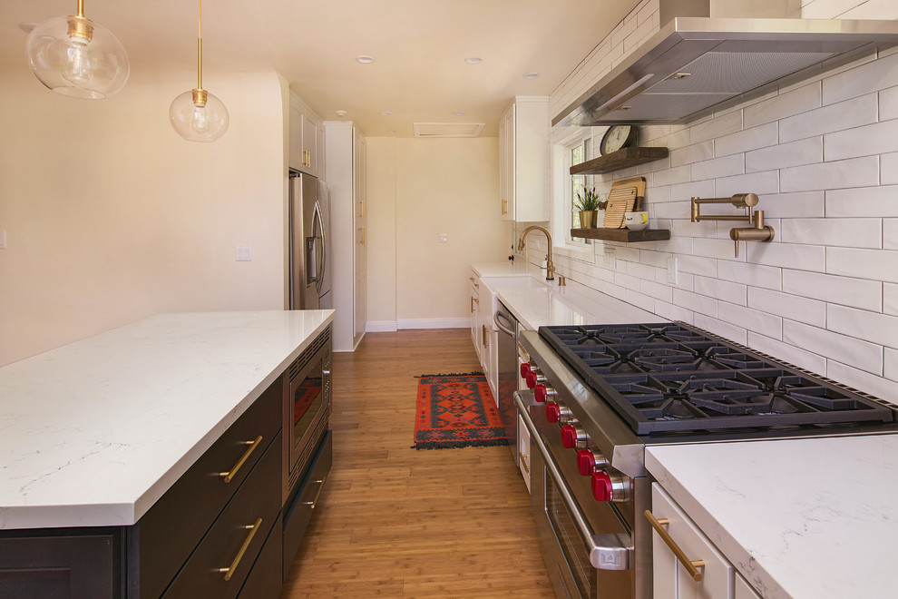 Mid-sized farmhouse single-wall light wood floor and brown floor open concept kitchen photo in Los Angeles with a farmhouse sink, shaker cabinets, white cabinets, quartz countertops, white backsplash, porcelain backsplash, stainless steel appliances, an island and yellow countertops