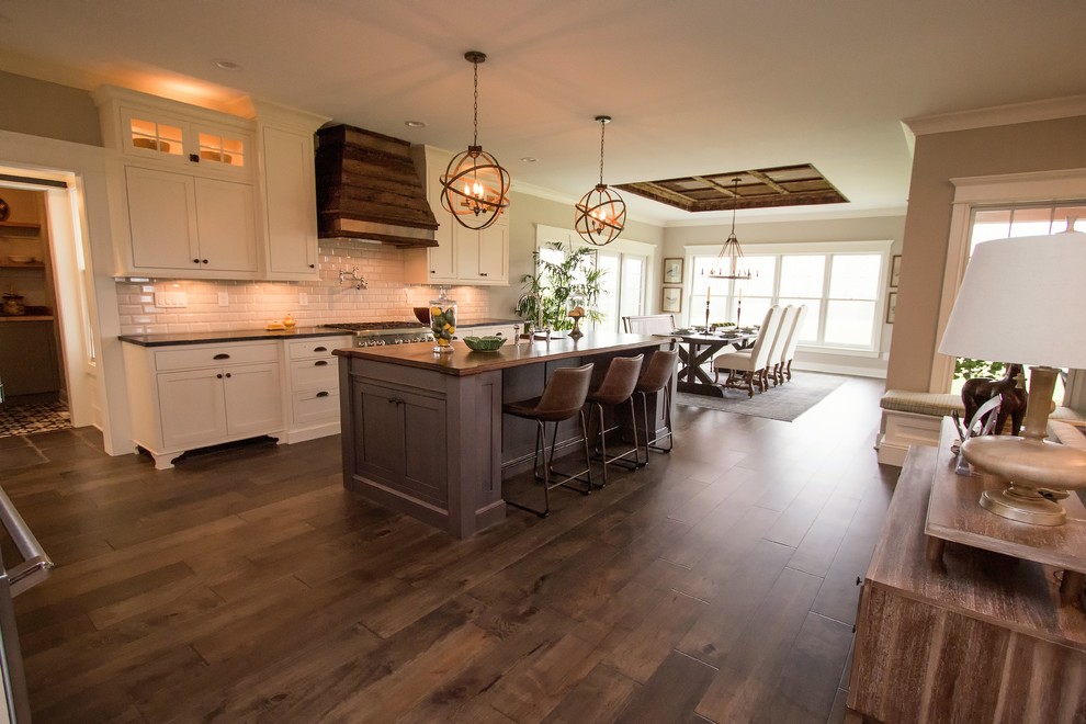 Inspiration for a large country l-shaped dark wood floor open concept kitchen remodel in Boston with a farmhouse sink, recessed-panel cabinets, white cabinets, solid surface countertops, gray backsplash, subway tile backsplash, stainless steel appliances and an island