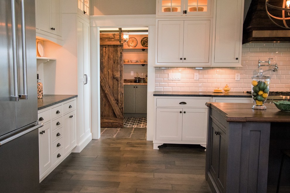 Large farmhouse l-shaped open plan kitchen in Boston with a belfast sink, recessed-panel cabinets, white cabinets, composite countertops, grey splashback, metro tiled splashback, stainless steel appliances, dark hardwood flooring and an island.
