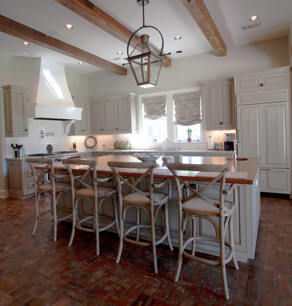 This is an example of a large farmhouse l-shaped kitchen in New Orleans with beaded cabinets, an island, white cabinets, granite worktops, white splashback, metro tiled splashback, integrated appliances, brick flooring and red floors.