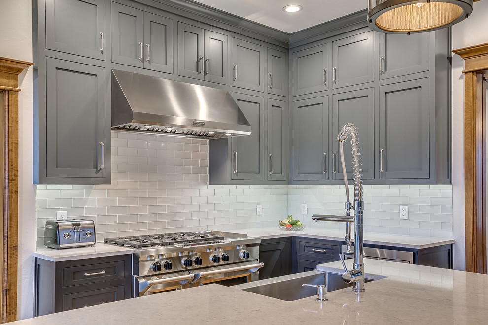 Example of a mid-sized farmhouse medium tone wood floor open concept kitchen design in Oklahoma City with a farmhouse sink, shaker cabinets, gray cabinets, quartz countertops, metallic backsplash, glass tile backsplash, stainless steel appliances and an island