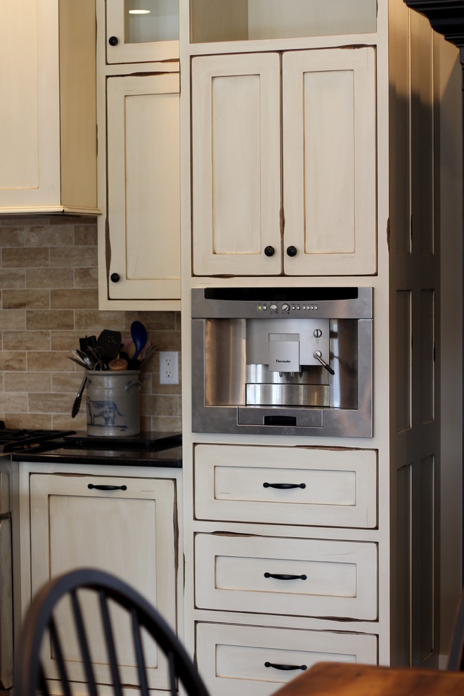 Photo of a farmhouse l-shaped kitchen/diner in Indianapolis with a belfast sink, shaker cabinets, distressed cabinets, quartz worktops, beige splashback, ceramic splashback, stainless steel appliances, medium hardwood flooring and a breakfast bar.