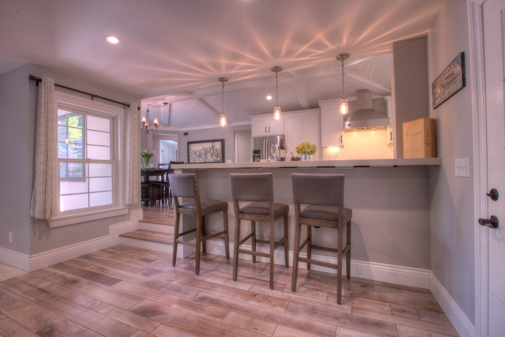 Bild på ett mellanstort lantligt grå grått kök, med en enkel diskho, släta luckor, vita skåp, bänkskiva i kvarts, vitt stänkskydd, stänkskydd i keramik, rostfria vitvaror, mellanmörkt trägolv, en halv köksö och grått golv