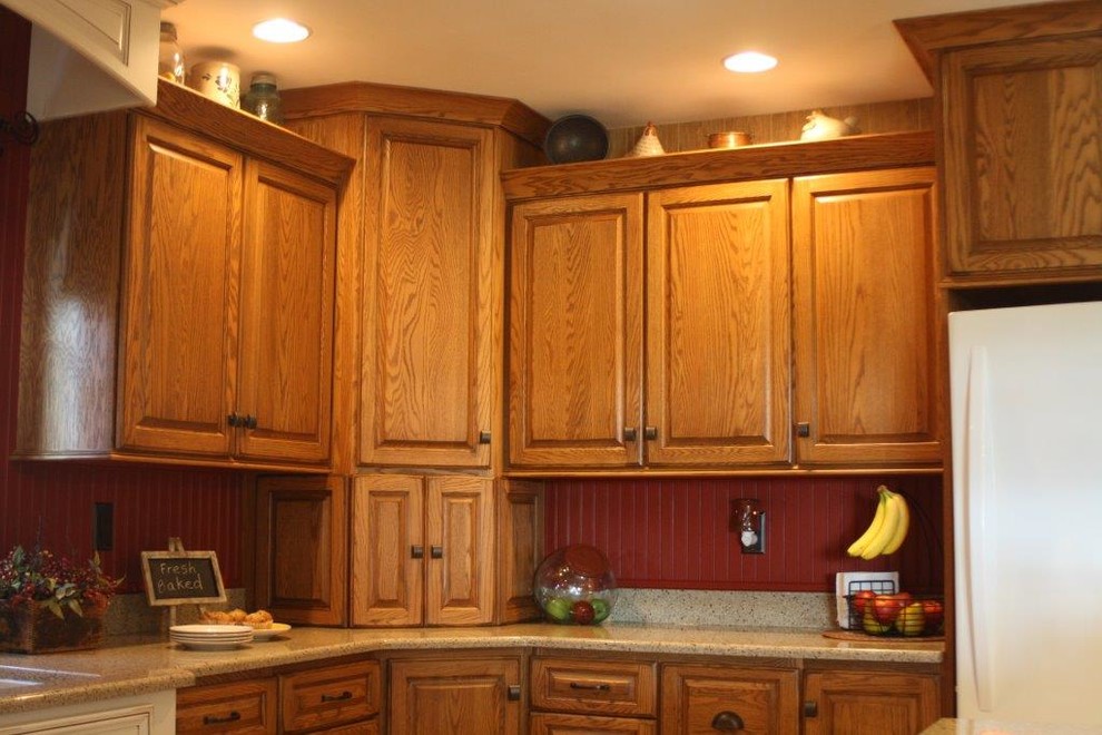 Lantlig inredning av ett litet kök, med en undermonterad diskho, luckor med upphöjd panel, skåp i mellenmörkt trä, granitbänkskiva, rött stänkskydd, stänkskydd i trä, vita vitvaror, vinylgolv och en köksö