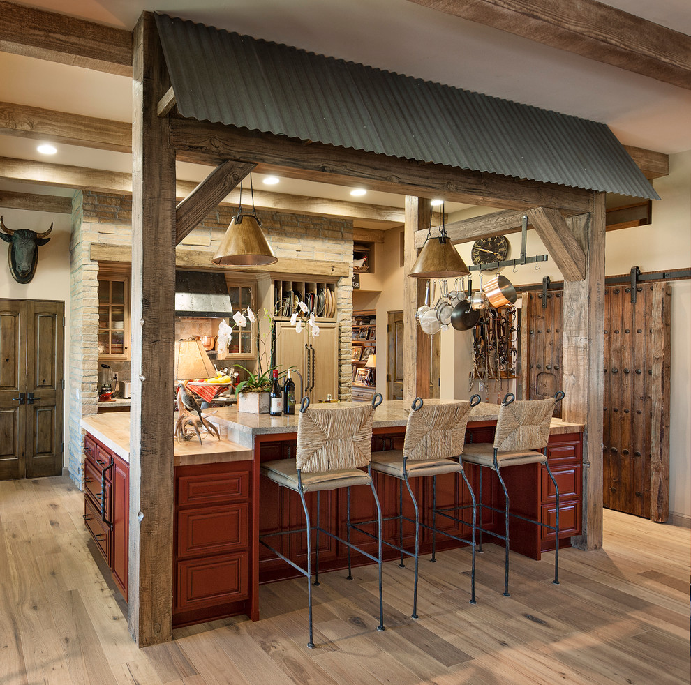 Cette photo montre une cuisine parallèle et encastrable sud-ouest américain en bois brun de taille moyenne avec un placard à porte affleurante, une crédence en carrelage de pierre, un sol en bois brun et îlot.