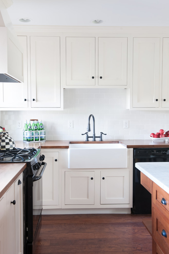 Cottage dark wood floor kitchen photo in Burlington with a farmhouse sink, white cabinets, wood countertops, white backsplash, subway tile backsplash and black appliances