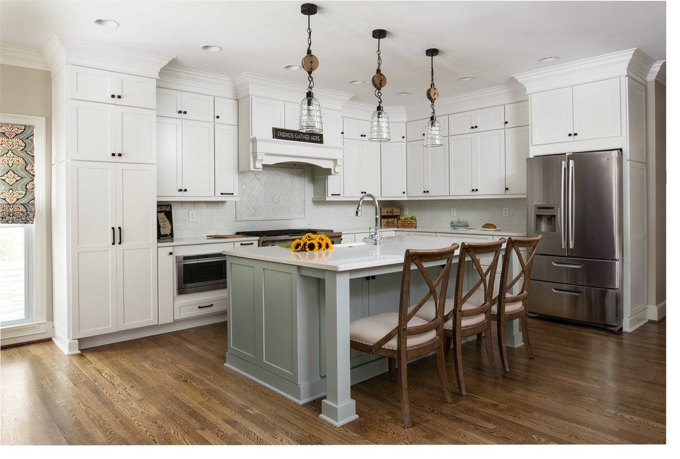 Photo of a large rural l-shaped kitchen/diner in Atlanta with a belfast sink, shaker cabinets, white cabinets, engineered stone countertops, white splashback, stainless steel appliances, medium hardwood flooring, an island and brown floors.
