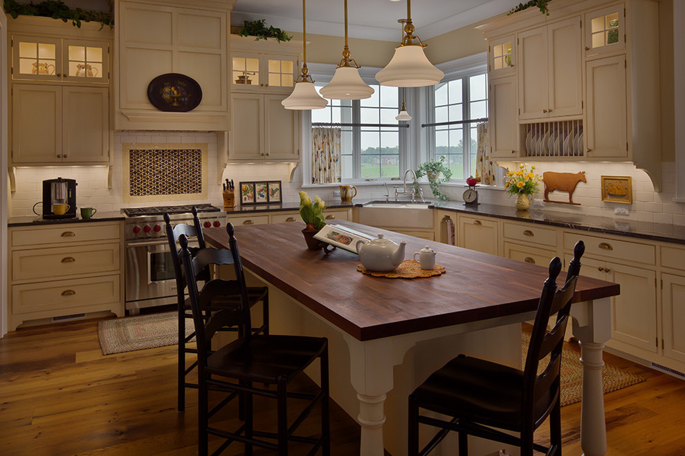 Example of a large farmhouse u-shaped medium tone wood floor eat-in kitchen design in Detroit with a farmhouse sink, flat-panel cabinets, white cabinets, granite countertops, white backsplash, subway tile backsplash, an island and stainless steel appliances