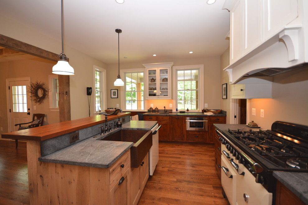 Example of a large cottage galley medium tone wood floor eat-in kitchen design in DC Metro with a farmhouse sink, recessed-panel cabinets, light wood cabinets, soapstone countertops, beige backsplash, white appliances and an island