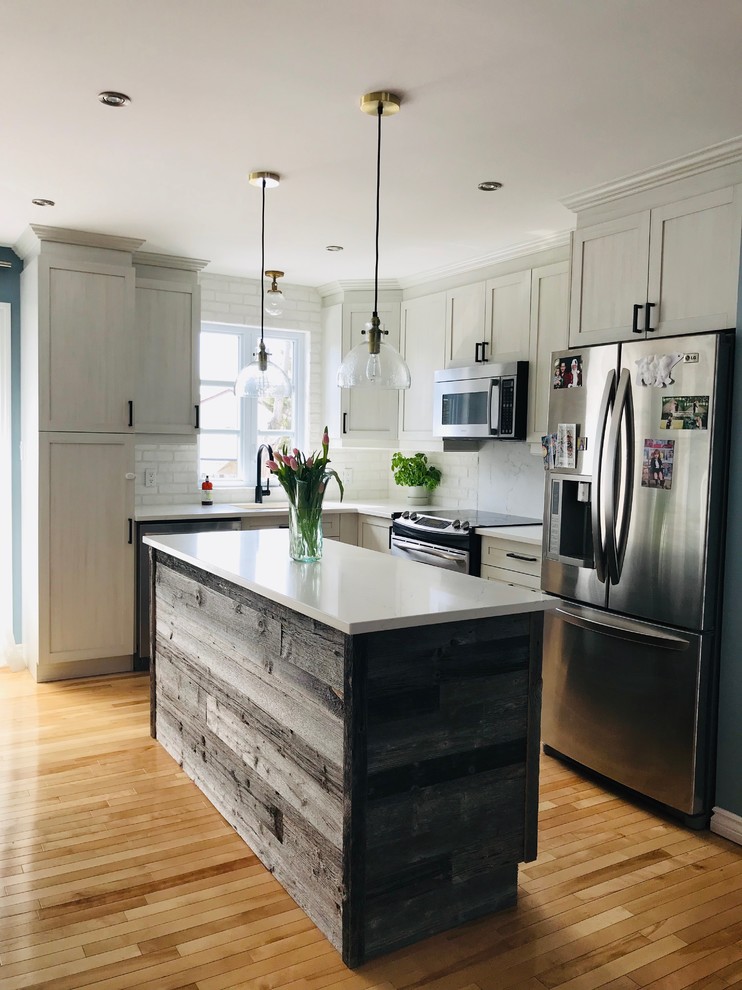 Photo of a small country l-shaped kitchen/diner in Montreal with a submerged sink, shaker cabinets, light wood cabinets, quartz worktops, white splashback, brick splashback, stainless steel appliances, light hardwood flooring, an island, beige floors and white worktops.