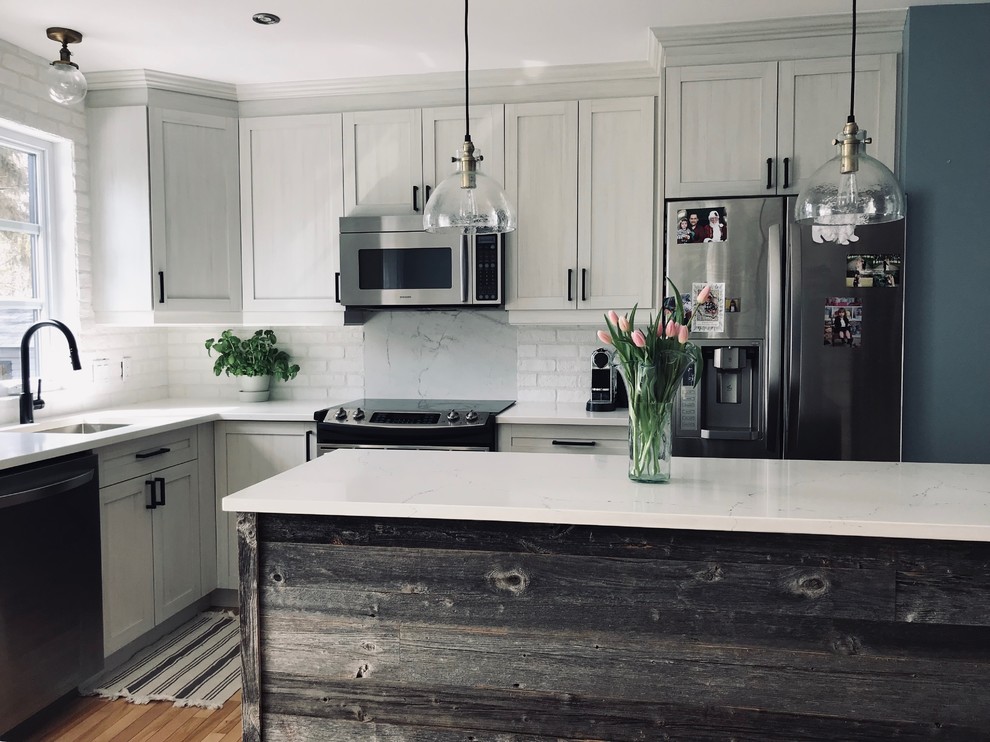 Photo of a small farmhouse l-shaped kitchen/diner in Montreal with a submerged sink, shaker cabinets, light wood cabinets, quartz worktops, white splashback, brick splashback, stainless steel appliances, light hardwood flooring, an island, beige floors and white worktops.
