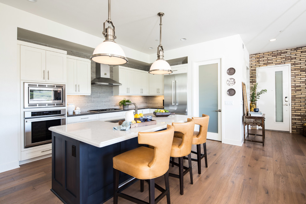 Photo of a traditional l-shaped kitchen in San Diego with shaker cabinets, white cabinets, grey splashback, stainless steel appliances, light hardwood flooring, an island and beige floors.