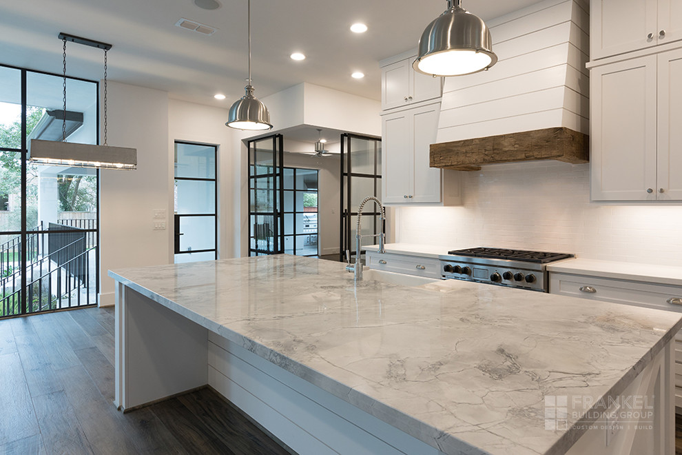 Large transitional single-wall medium tone wood floor and brown floor open concept kitchen photo in Houston with a farmhouse sink, white cabinets, white backsplash, subway tile backsplash, stainless steel appliances, an island and gray countertops