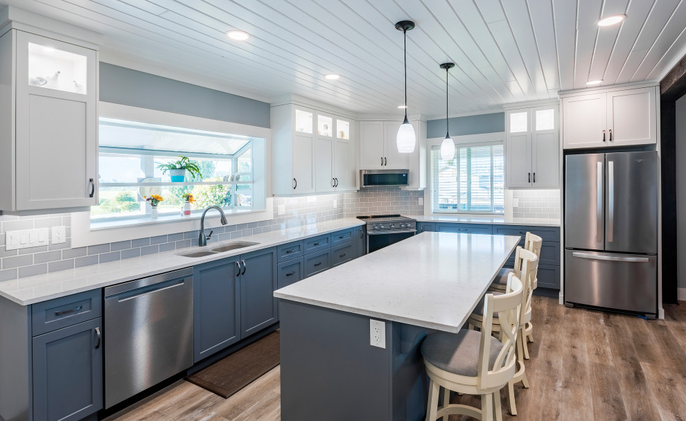 Mid-sized elegant l-shaped vinyl floor and brown floor open concept kitchen photo in Vancouver with an undermount sink, shaker cabinets, blue cabinets, quartz countertops, blue backsplash, subway tile backsplash, stainless steel appliances, an island and white countertops