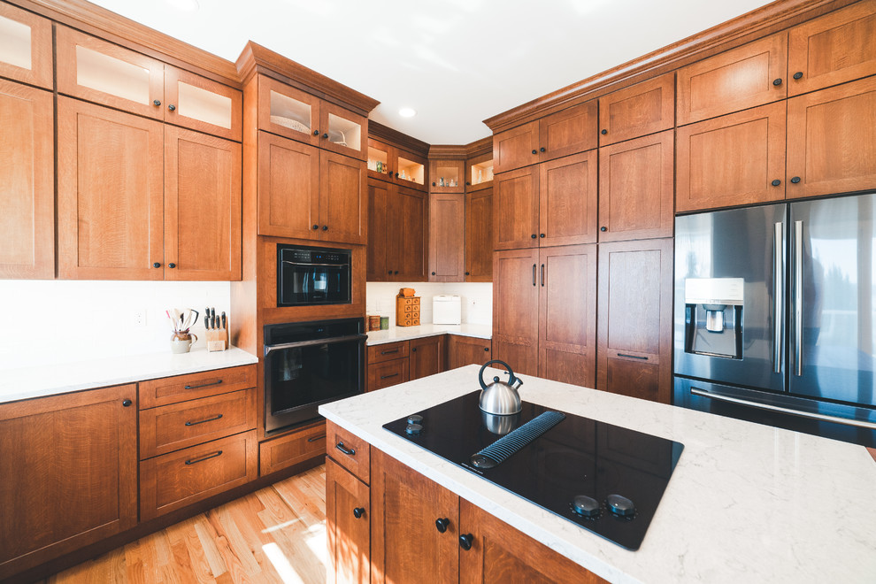 シアトルにある高級な中くらいなカントリー風のおしゃれなキッチン (エプロンフロントシンク、落し込みパネル扉のキャビネット、中間色木目調キャビネット、珪岩カウンター、白いキッチンパネル、サブウェイタイルのキッチンパネル、黒い調理設備、無垢フローリング、茶色い床、白いキッチンカウンター) の写真