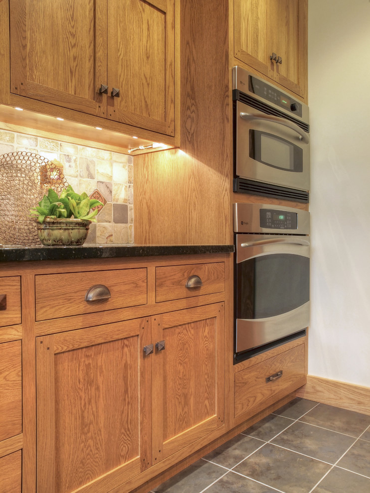 Amerikansk inredning av ett mellanstort l-kök, med en undermonterad diskho, skåp i shakerstil, skåp i ljust trä, bänkskiva i koppar, stänkskydd i stenkakel, rostfria vitvaror, en köksö och grått golv
