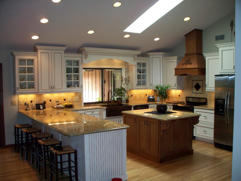 Klassisk inredning av ett stort kök, med en rustik diskho, luckor med infälld panel, vita skåp, granitbänkskiva, beige stänkskydd, stänkskydd i keramik, rostfria vitvaror, ljust trägolv och en köksö