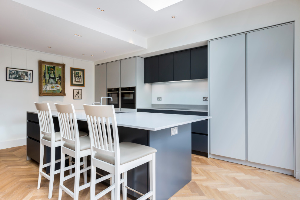 Contemporary kitchen in Sussex with a submerged sink, flat-panel cabinets, grey cabinets, black appliances, light hardwood flooring, an island, beige floors and grey worktops.