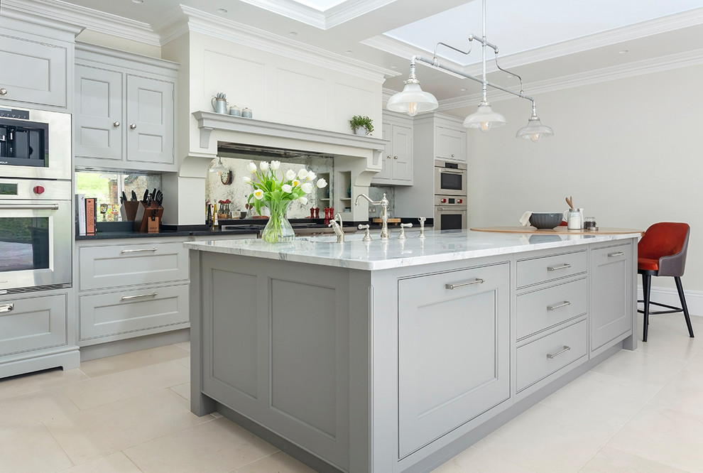Klassisk inredning av ett stort kök och matrum, med släta luckor, grå skåp, marmorbänkskiva, kalkstensgolv, en köksö och beiget golv