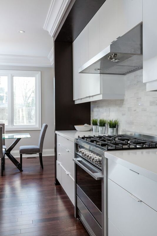 Photo of a classic kitchen in Toronto with flat-panel cabinets, white cabinets, engineered stone countertops, white splashback, stone tiled splashback, stainless steel appliances, medium hardwood flooring and an island.